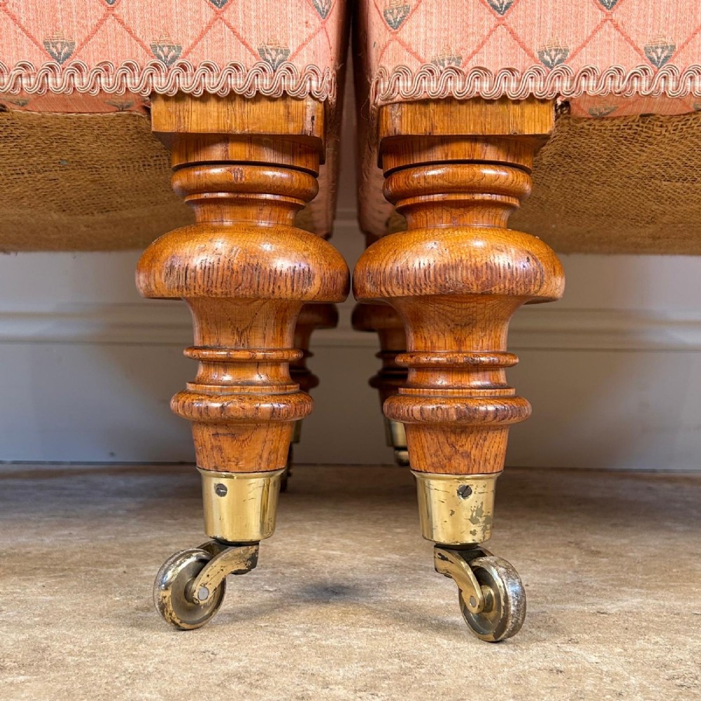 A pair of 19th-century corner armchairs upholstered in pink diamond-patterned fabric featuring button-tufted rounded backs and turned oak legs on brass castors. View VII