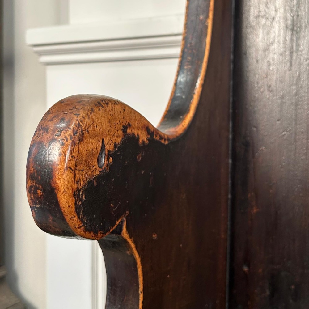 An eighteenth-century dark fruitwood tavern settle featuring a high vertical planked back, winged sides, and integrated under-seat drawers. View II
