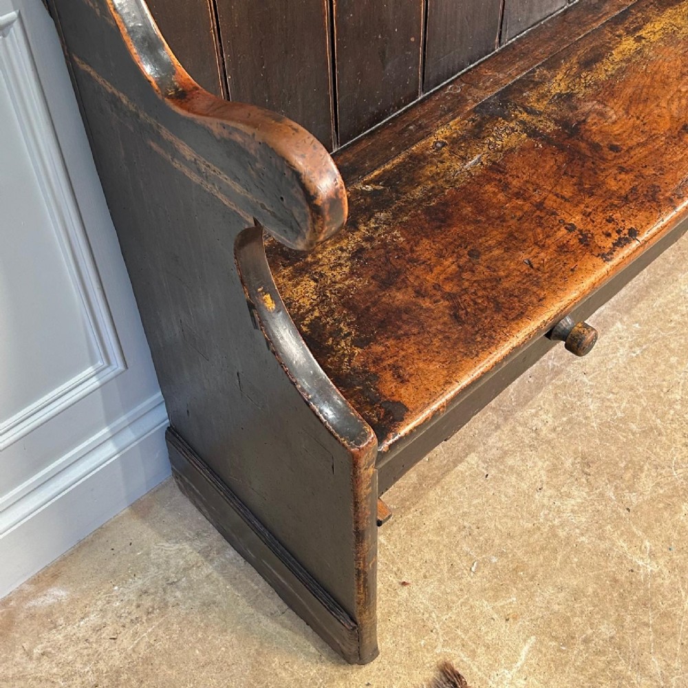 An eighteenth-century dark fruitwood tavern settle featuring a high vertical planked back, winged sides, and integrated under-seat drawers. View V