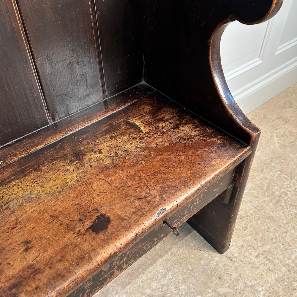 An eighteenth-century dark fruitwood tavern settle featuring a high vertical planked back, winged sides, and integrated under-seat drawers. View VI