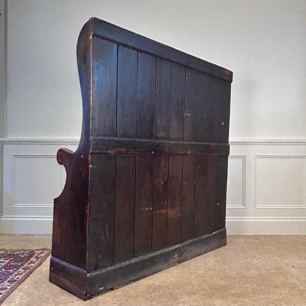 An eighteenth-century dark fruitwood tavern settle featuring a high vertical planked back, winged sides, and integrated under-seat drawers. View VII