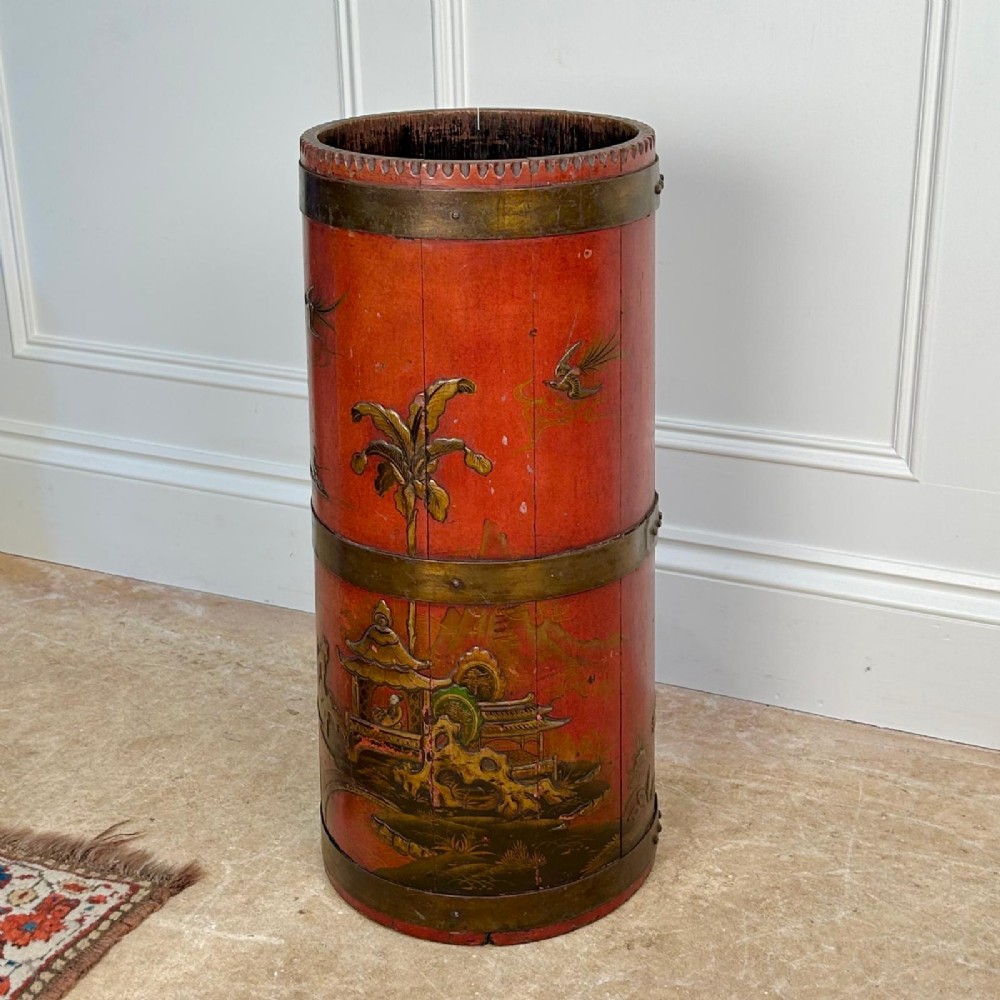 A cylindrical red Edwardian umbrella stand featuring hand-painted gold Chinoiserie scenes and bound by brass hoops. View II