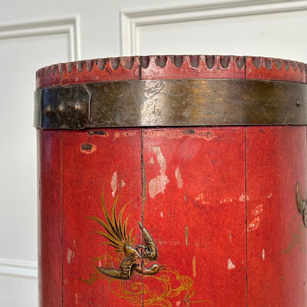 A cylindrical red Edwardian umbrella stand featuring hand-painted gold Chinoiserie scenes and bound by brass hoops. View III