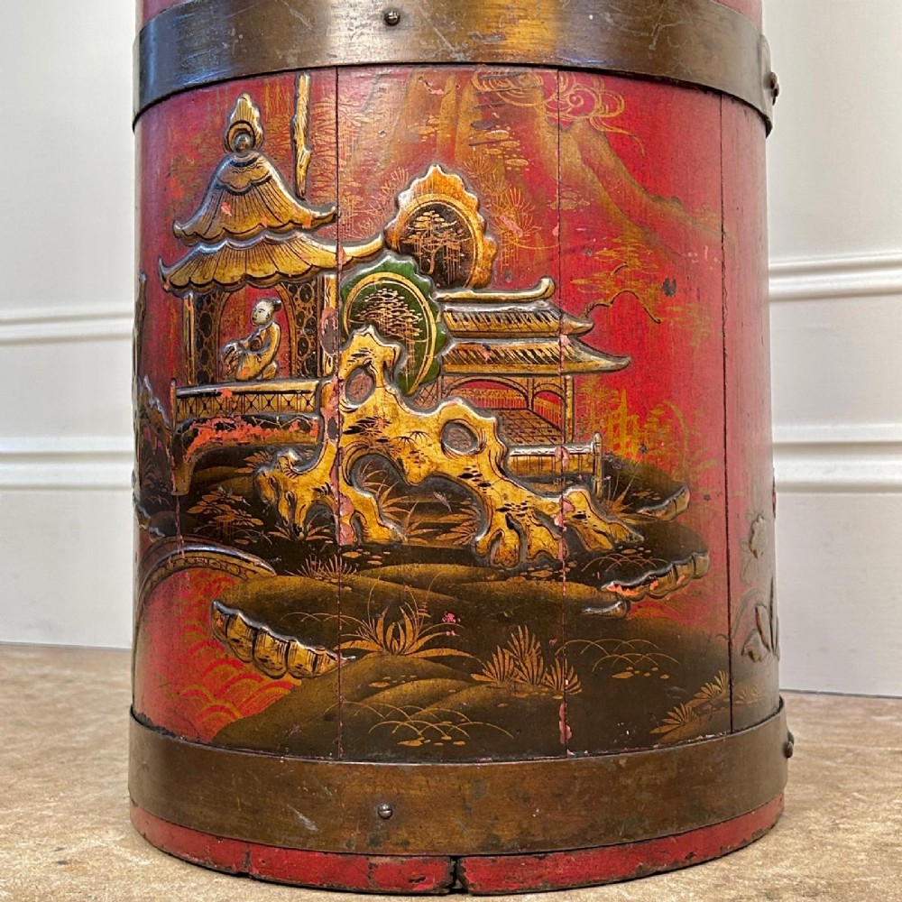 A cylindrical red Edwardian umbrella stand featuring hand-painted gold Chinoiserie scenes and bound by brass hoops. View V