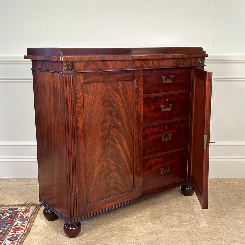 A George IV flame mahogany dwarf secretaire cabinet featuring reeded pilasters, two panelled doors, and turned bun feet. View II