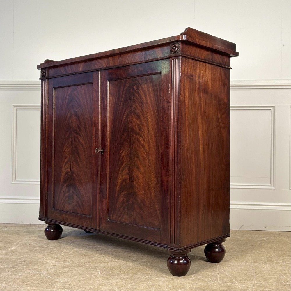 A George IV flame mahogany dwarf secretaire cabinet featuring reeded pilasters, two panelled doors, and turned bun feet. View V