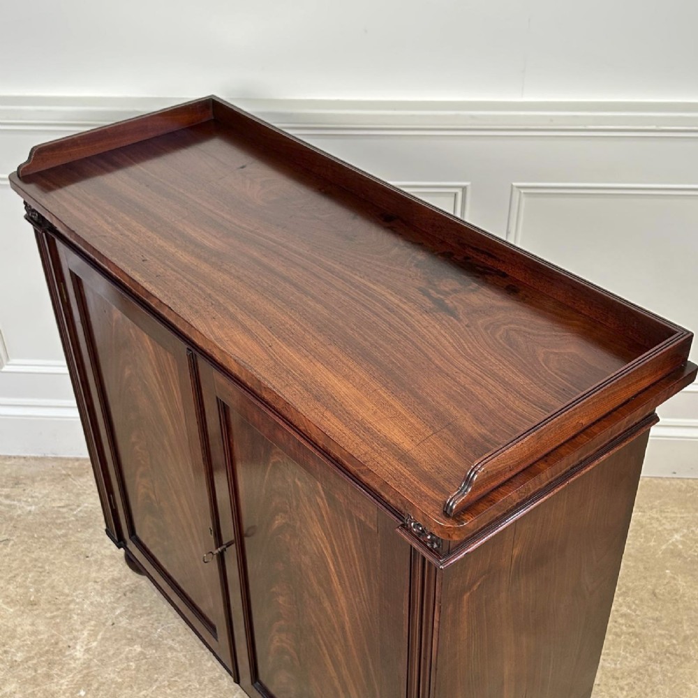 A George IV flame mahogany dwarf secretaire cabinet featuring reeded pilasters, two panelled doors, and turned bun feet. View VI