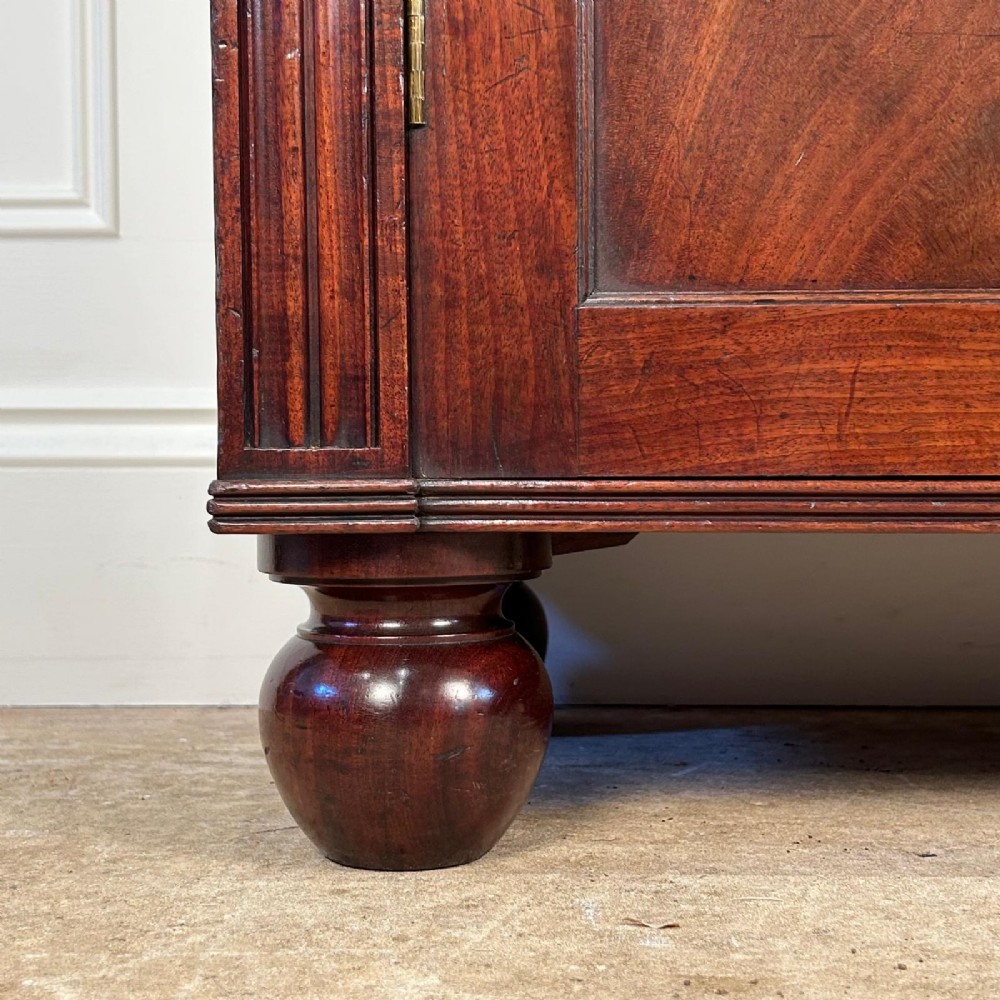 A George IV flame mahogany dwarf secretaire cabinet featuring reeded pilasters, two panelled doors, and turned bun feet. View VII