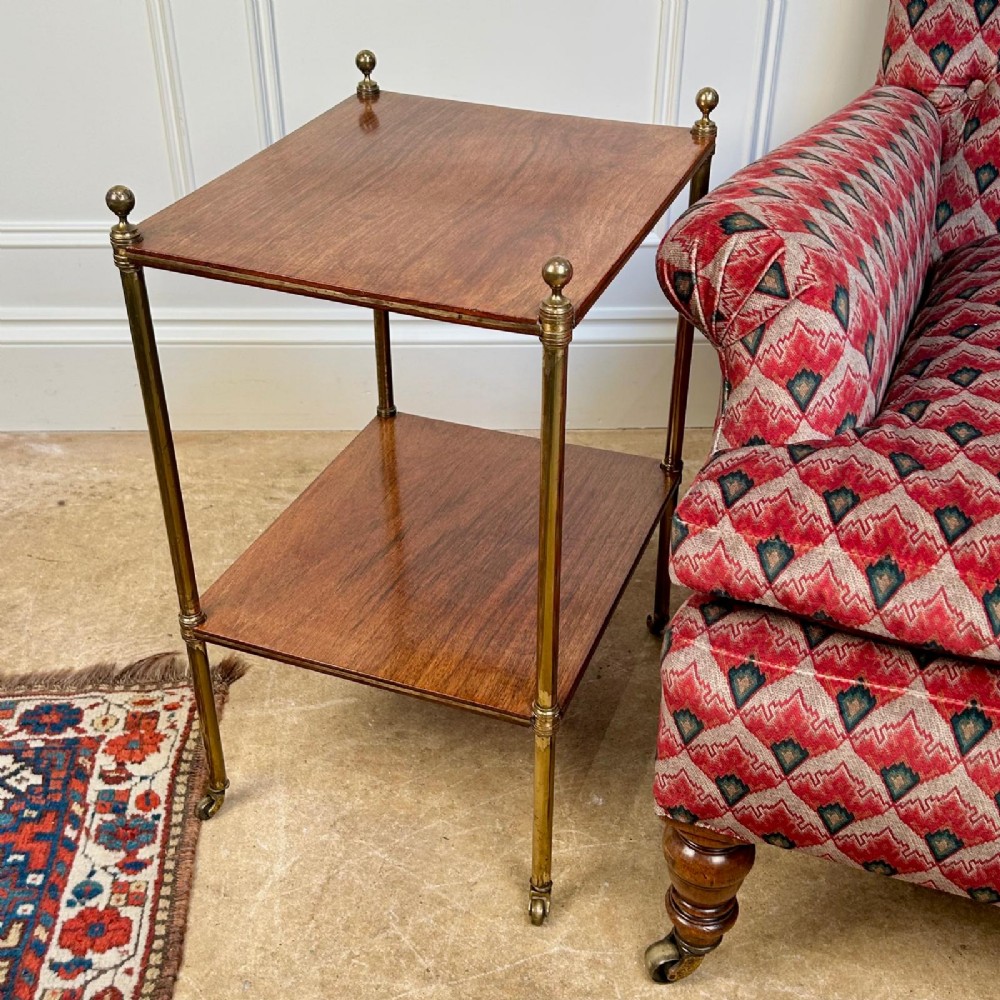 An Edwardian two-tier side table with polished square rosewood shelves held by slender brass legs with finials and castors. View II