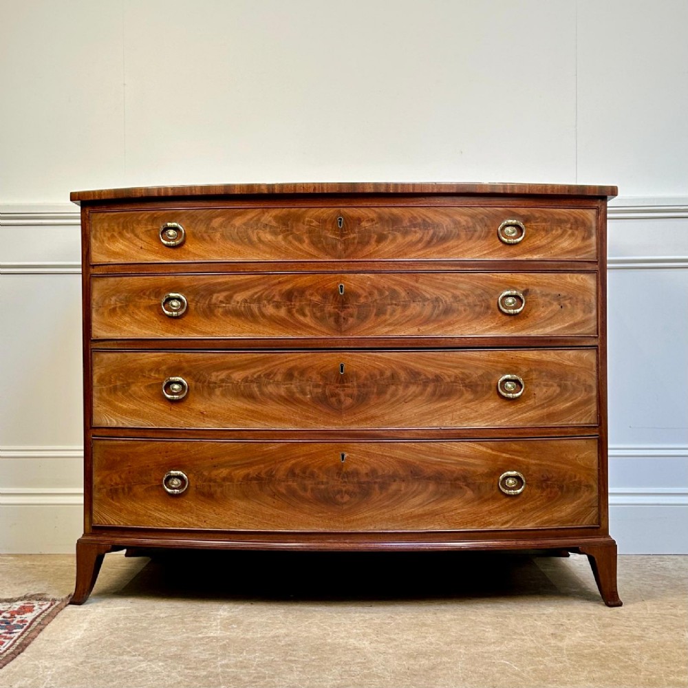 A late 18th-century Georgian flame mahogany bowfront chest of drawers featuring four graduated drawers with brass handles and splayed bracket feet.