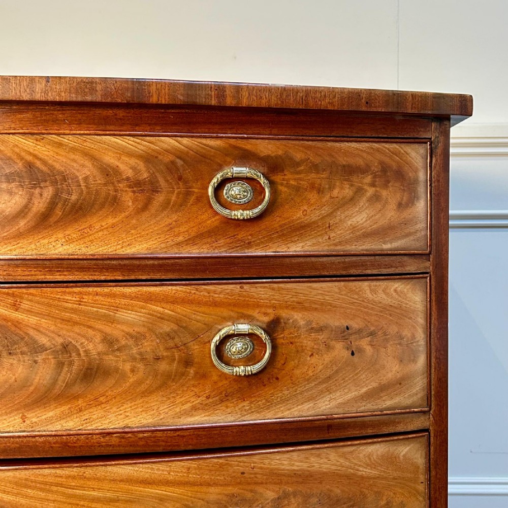 A late 18th-century Georgian flame mahogany bowfront chest of drawers featuring four graduated drawers with brass handles and splayed bracket feet. View IV