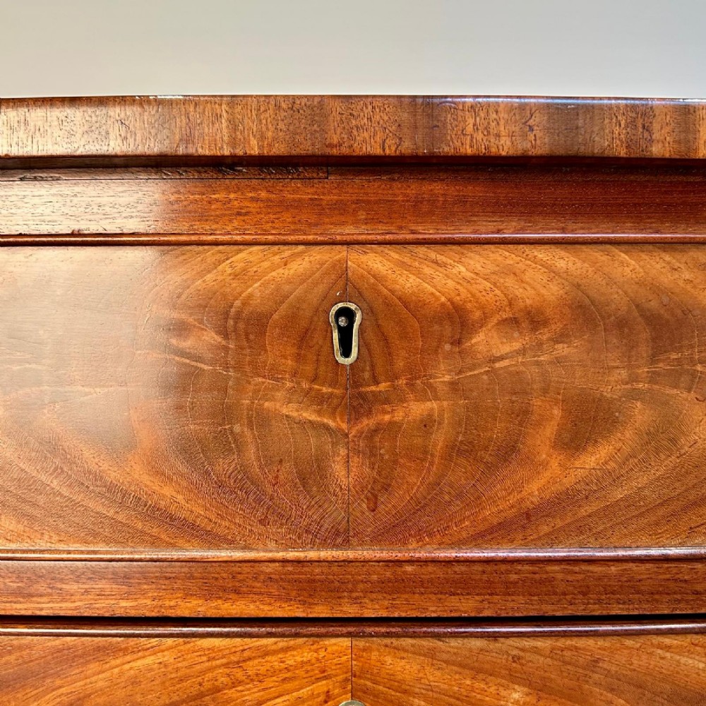 A late 18th-century Georgian flame mahogany bowfront chest of drawers featuring four graduated drawers with brass handles and splayed bracket feet. View VI