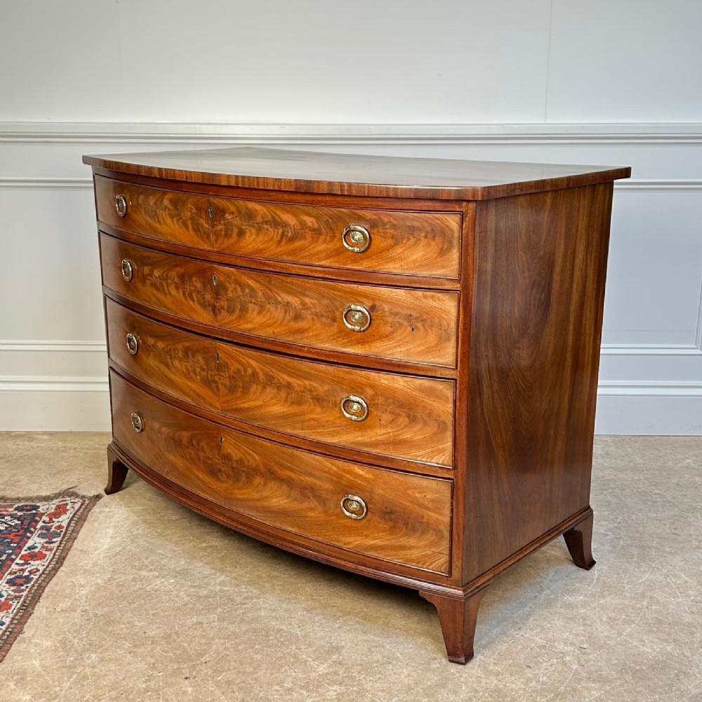 A late 18th-century Georgian flame mahogany bowfront chest of drawers featuring four graduated drawers with brass handles and splayed bracket feet. View VIII