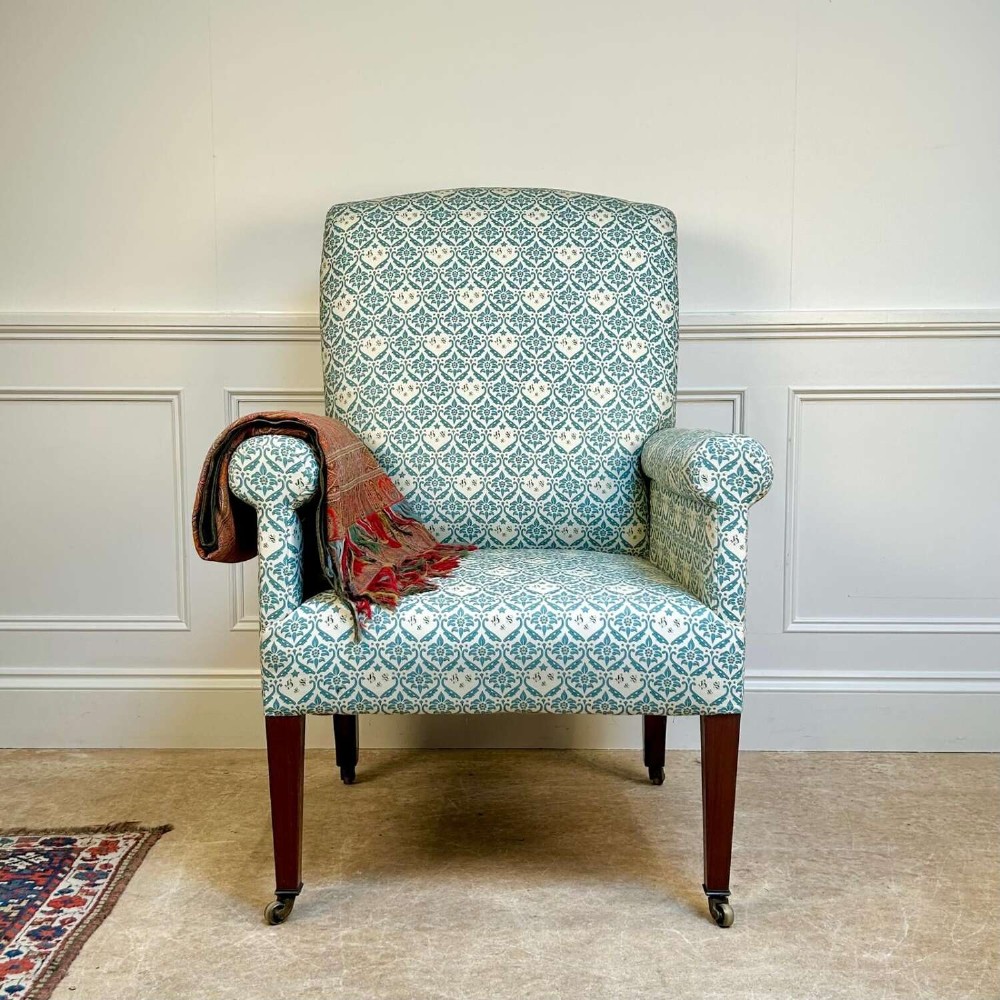 A high-backed Edwardian library armchair upholstered in a patterned blue and white fabric with mahogany legs and brass castors.