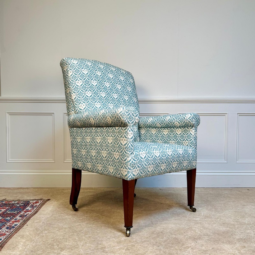 A high-backed Edwardian library armchair upholstered in a patterned blue and white fabric with mahogany legs and brass castors. View II