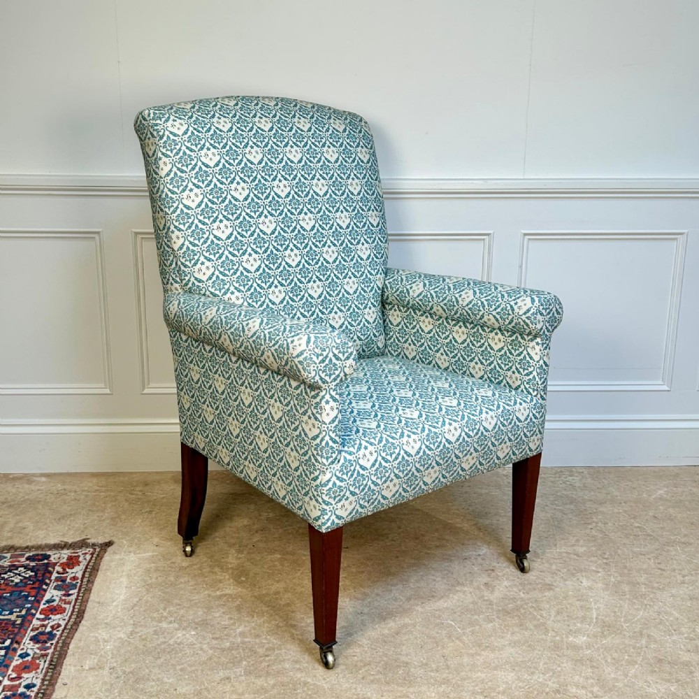 A high-backed Edwardian library armchair upholstered in a patterned blue and white fabric with mahogany legs and brass castors. View III