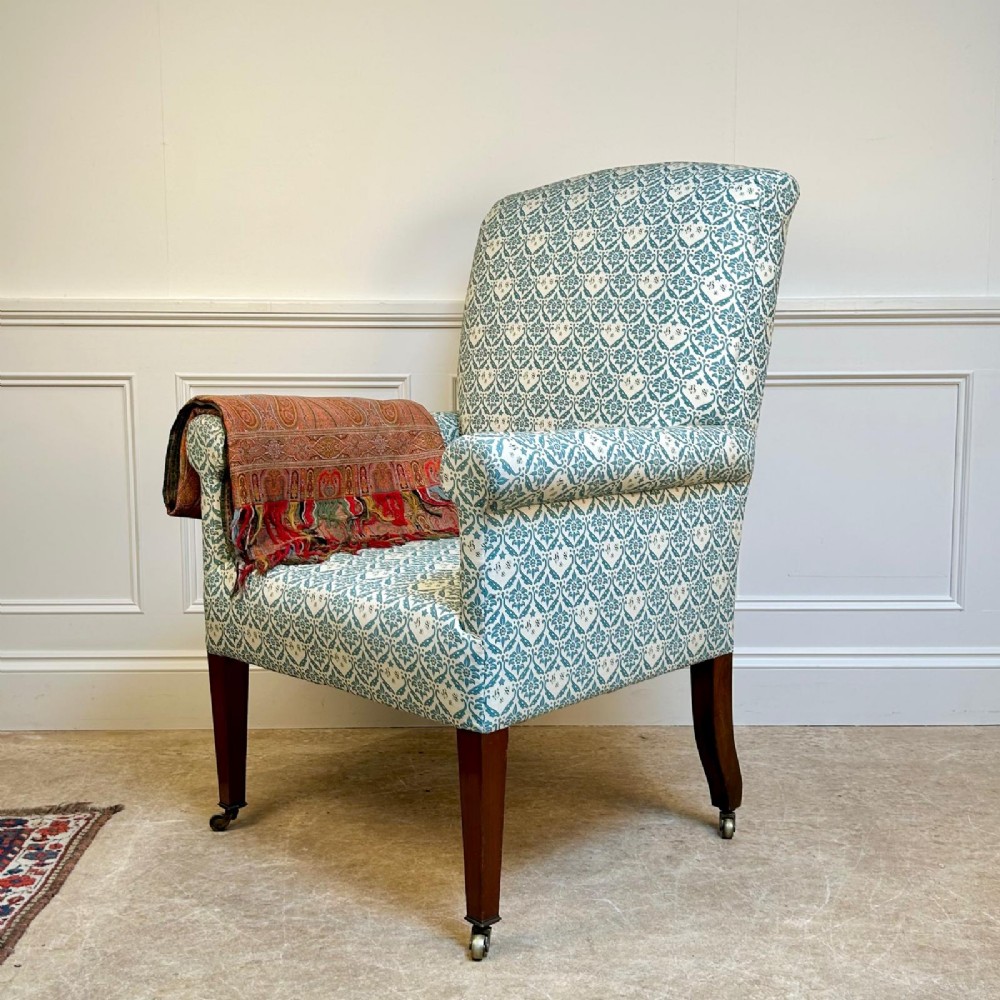 A high-backed Edwardian library armchair upholstered in a patterned blue and white fabric with mahogany legs and brass castors. View IV