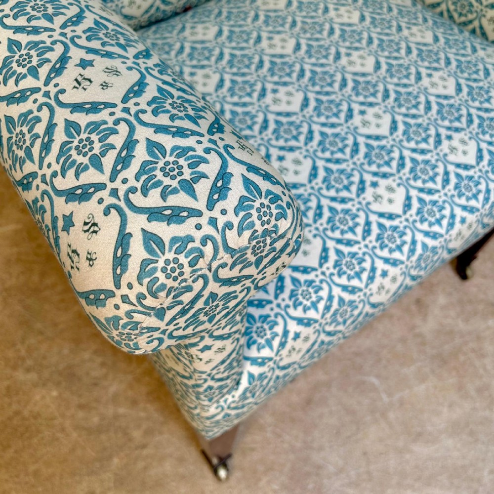 A high-backed Edwardian library armchair upholstered in a patterned blue and white fabric with mahogany legs and brass castors. View V