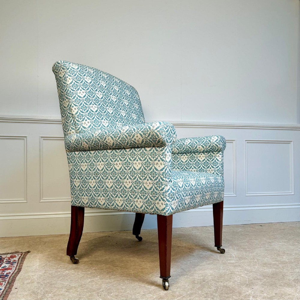 A high-backed Edwardian library armchair upholstered in a patterned blue and white fabric with mahogany legs and brass castors. View VI