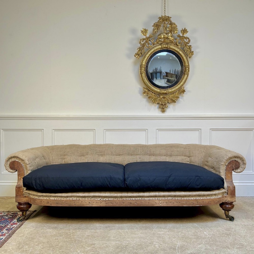 A nineteenth-century country house sofa featuring a buttoned hessian back, dark navy seat cushions, rolled arms, and turned wooden legs on brass castors. View II