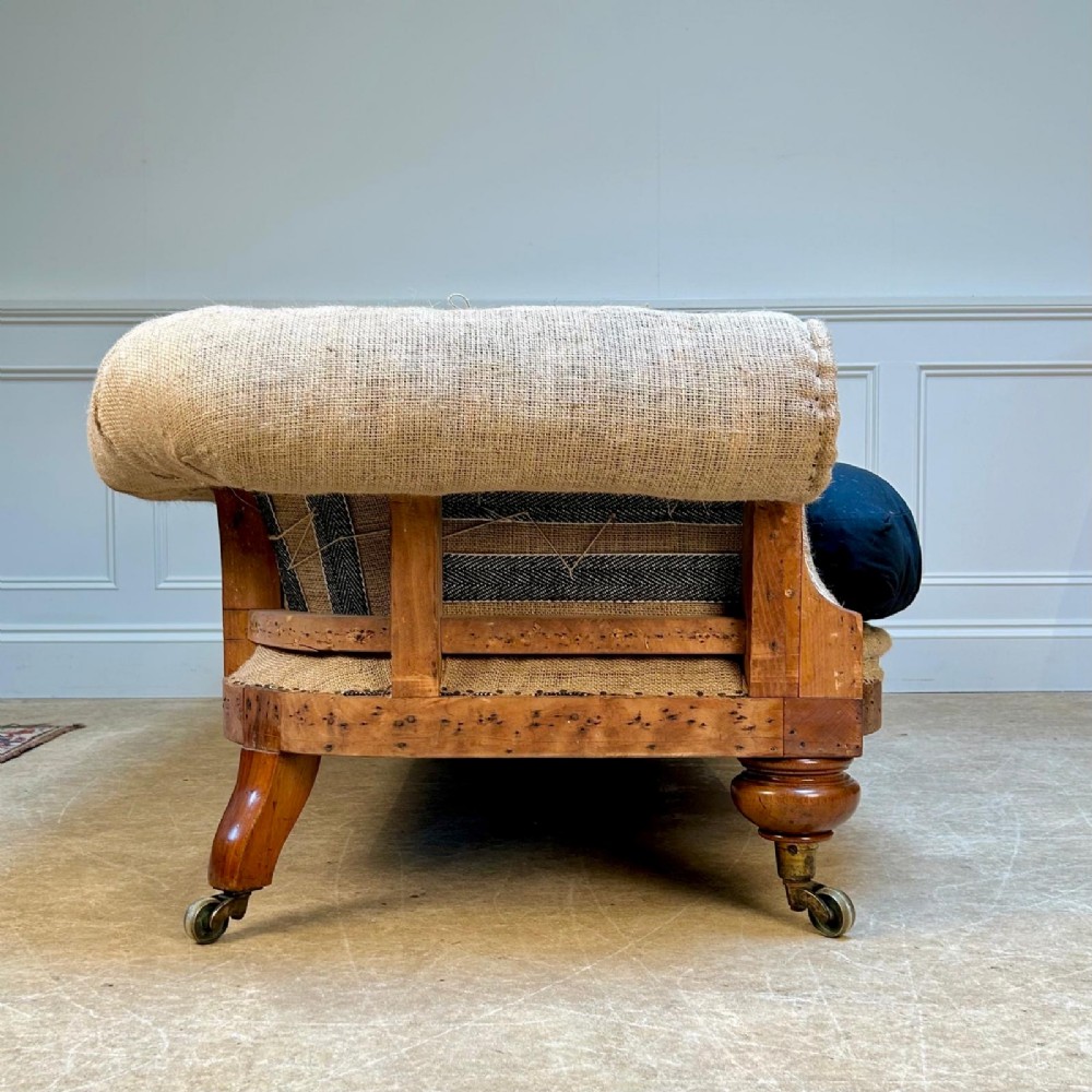 A nineteenth-century country house sofa featuring a buttoned hessian back, dark navy seat cushions, rolled arms, and turned wooden legs on brass castors. View III