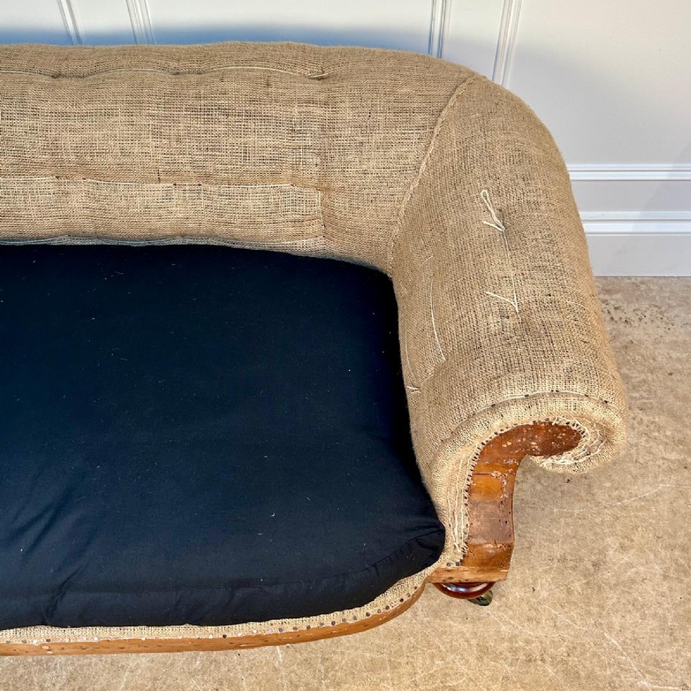 A nineteenth-century country house sofa featuring a buttoned hessian back, dark navy seat cushions, rolled arms, and turned wooden legs on brass castors. View V