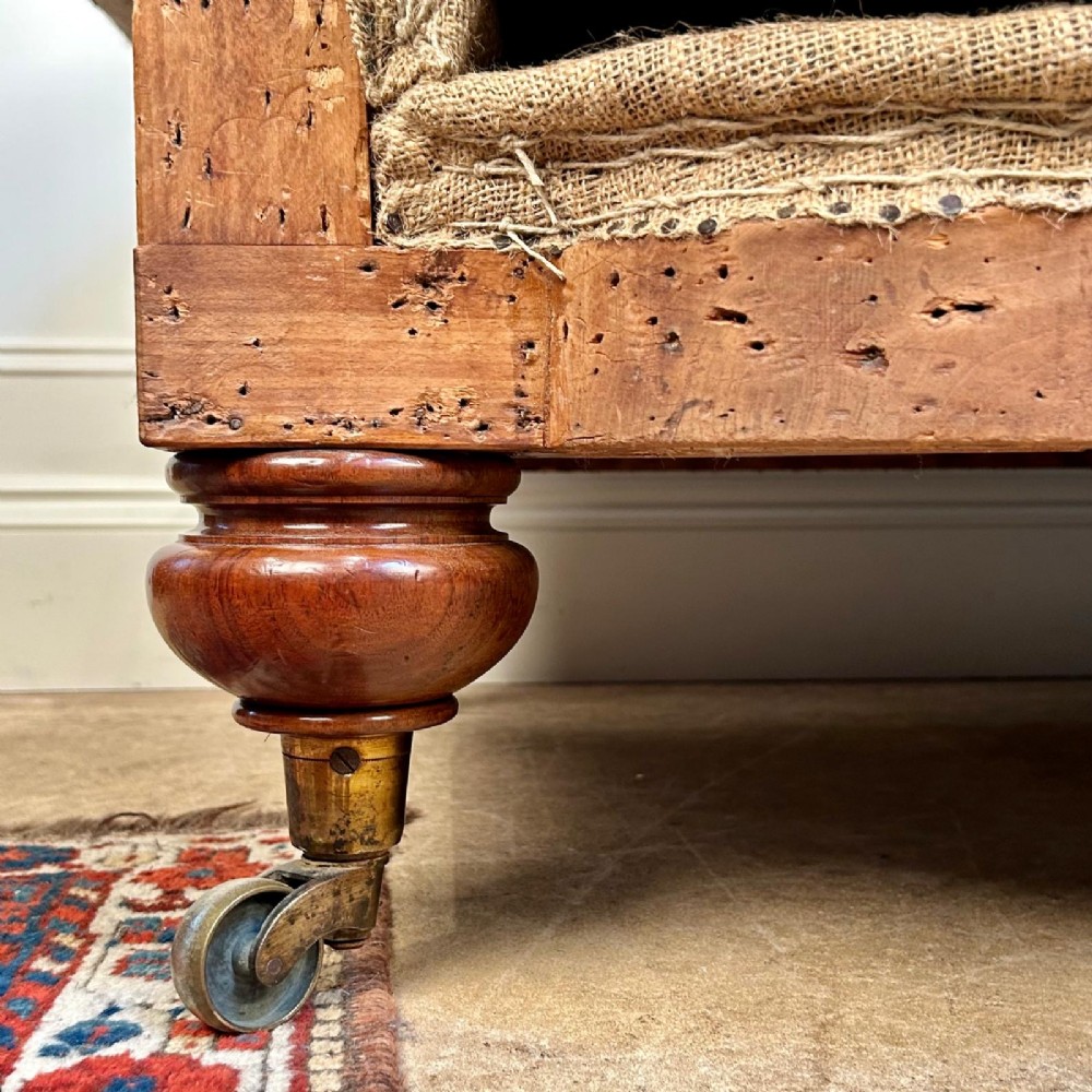 A nineteenth-century country house sofa featuring a buttoned hessian back, dark navy seat cushions, rolled arms, and turned wooden legs on brass castors. View VI