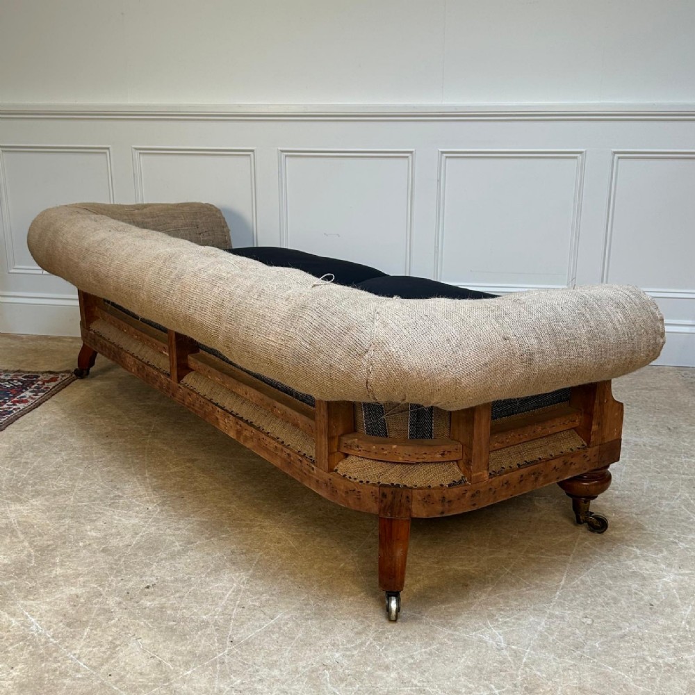 A nineteenth-century country house sofa featuring a buttoned hessian back, dark navy seat cushions, rolled arms, and turned wooden legs on brass castors. View VII
