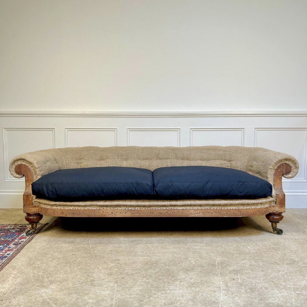 A nineteenth-century country house sofa featuring a buttoned hessian back, dark navy seat cushions, rolled arms, and turned wooden legs on brass castors. View VIII