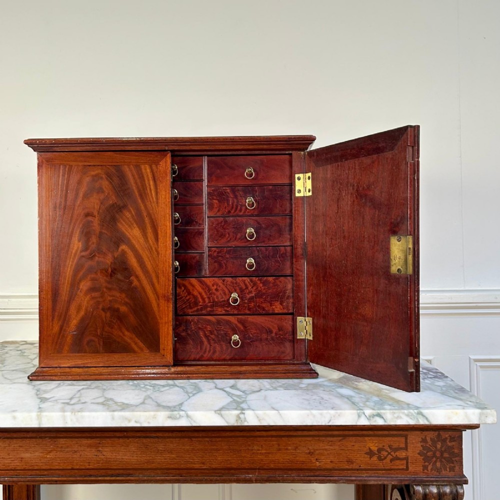 An 18th-century mahogany tabletop collectors cabinet featuring double doors that open to reveal multiple graduated internal drawers with small brass ring handles.