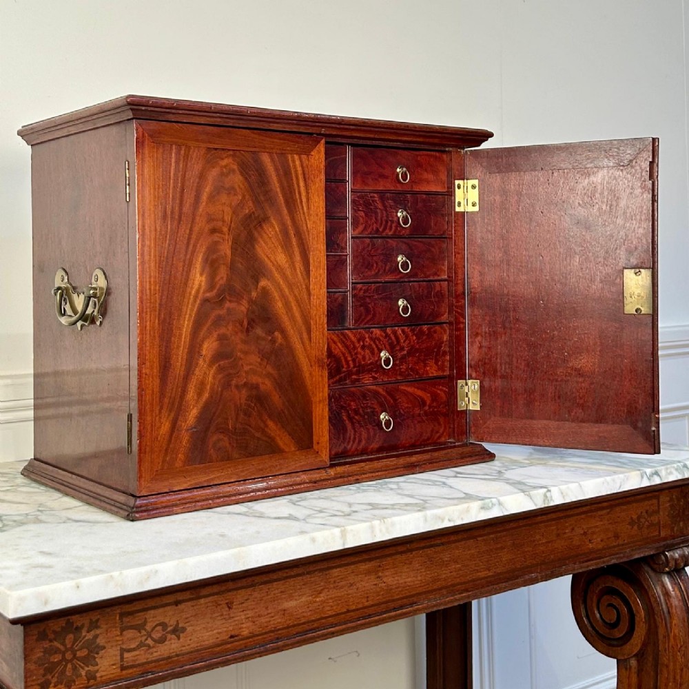An 18th-century mahogany tabletop collectors cabinet featuring double doors that open to reveal multiple graduated internal drawers with small brass ring handles. View II