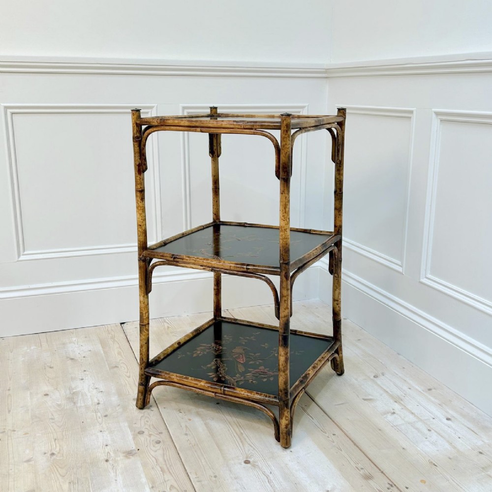 A three-tiered bamboo etagere featuring dark lacquered square shelf panels painted with bird and botanical designs.
