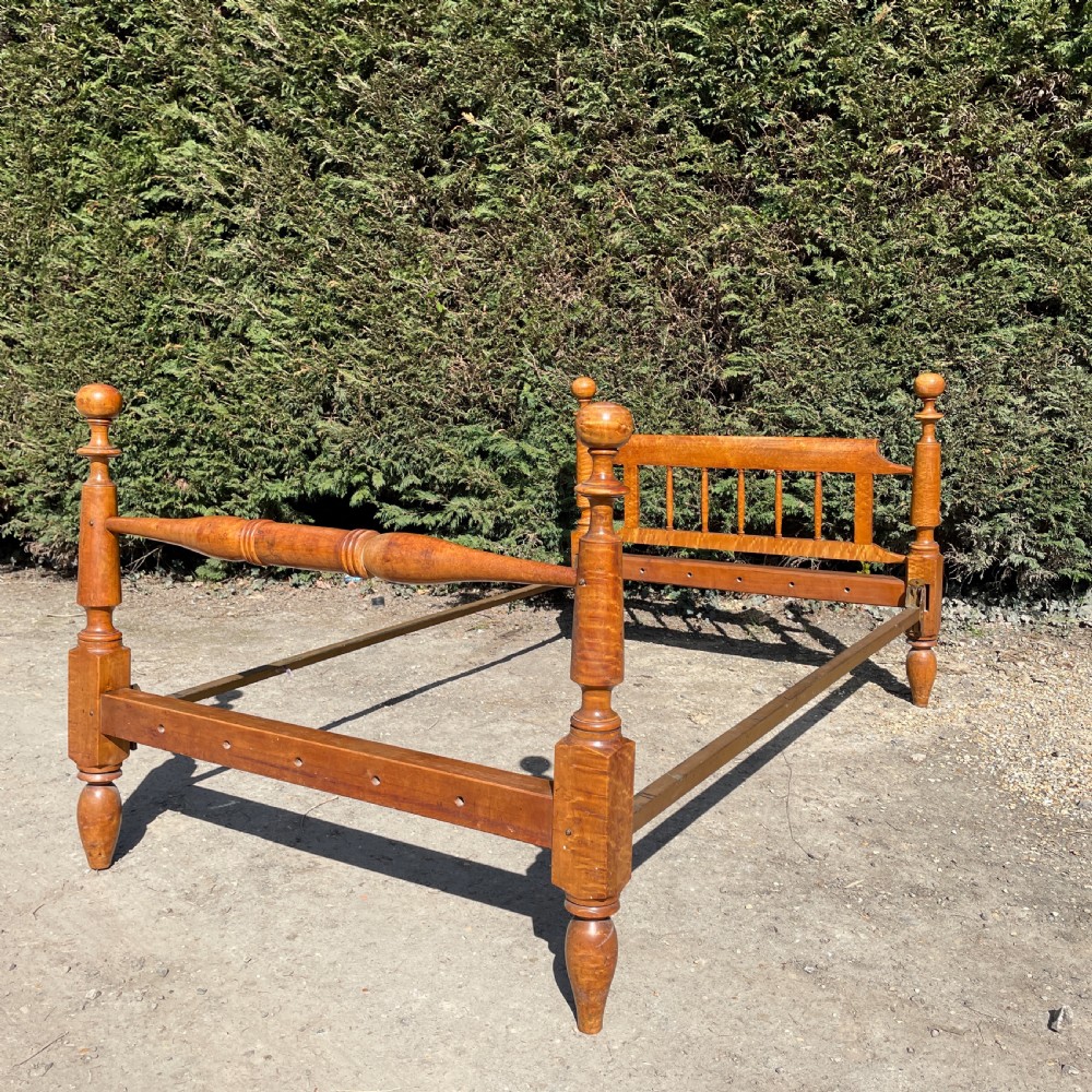 An early nineteenth-century American Federal bedstead constructed from figured tiger maple wood featuring four turned posts, cannonball finials, and a spindle headboard.