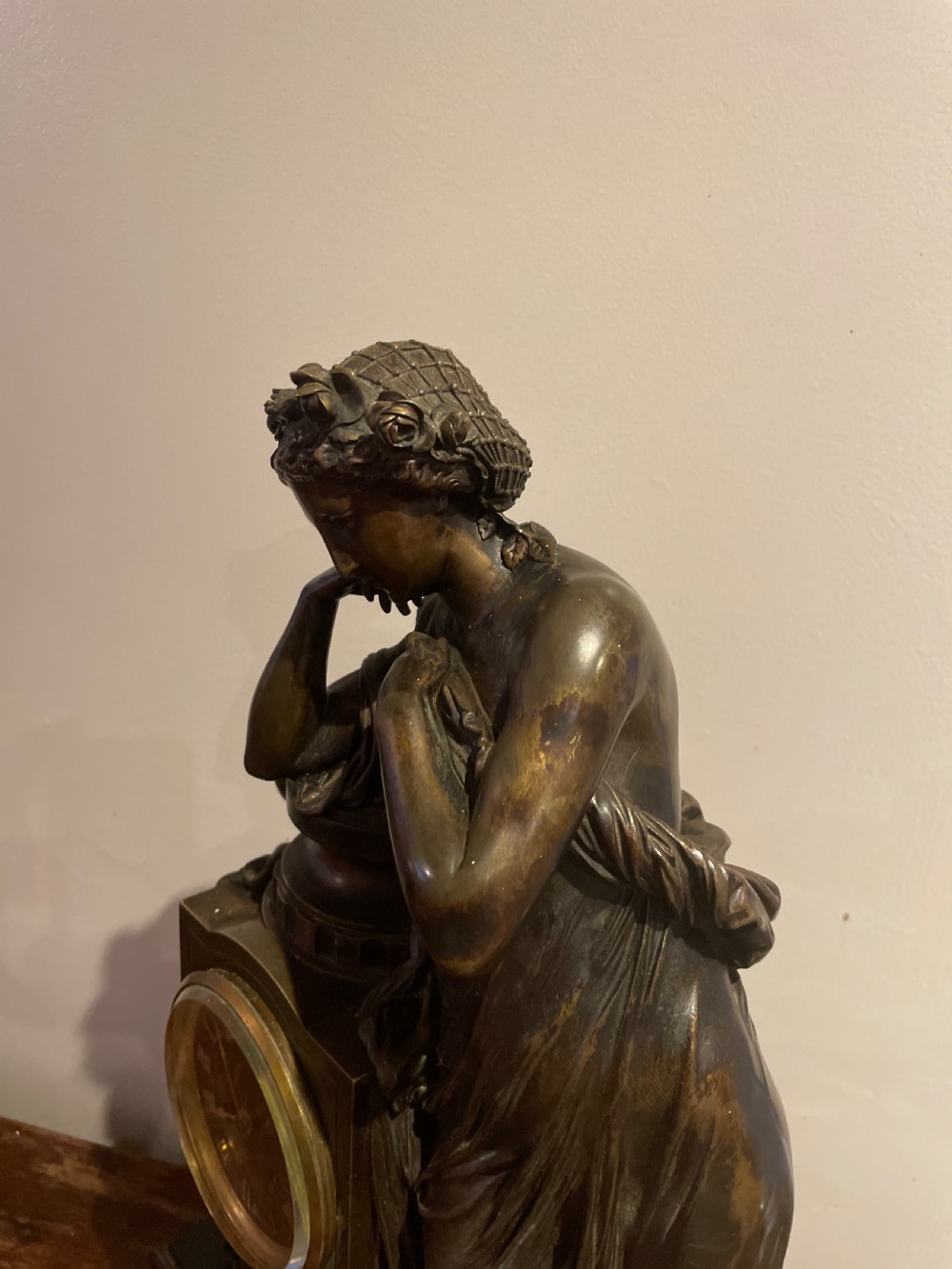 A late 19th-century French dark patinated bronze mantel clock depicting a classical draped female figure leaning upon a column containing a round dial with Roman numerals. View III