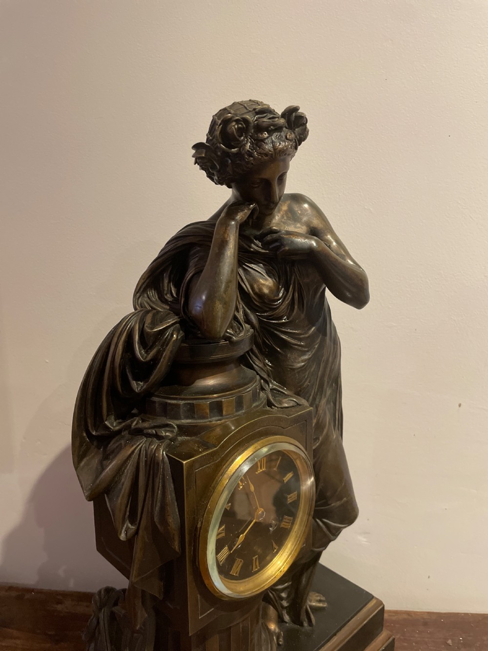 A late 19th-century French dark patinated bronze mantel clock depicting a classical draped female figure leaning upon a column containing a round dial with Roman numerals. View IV