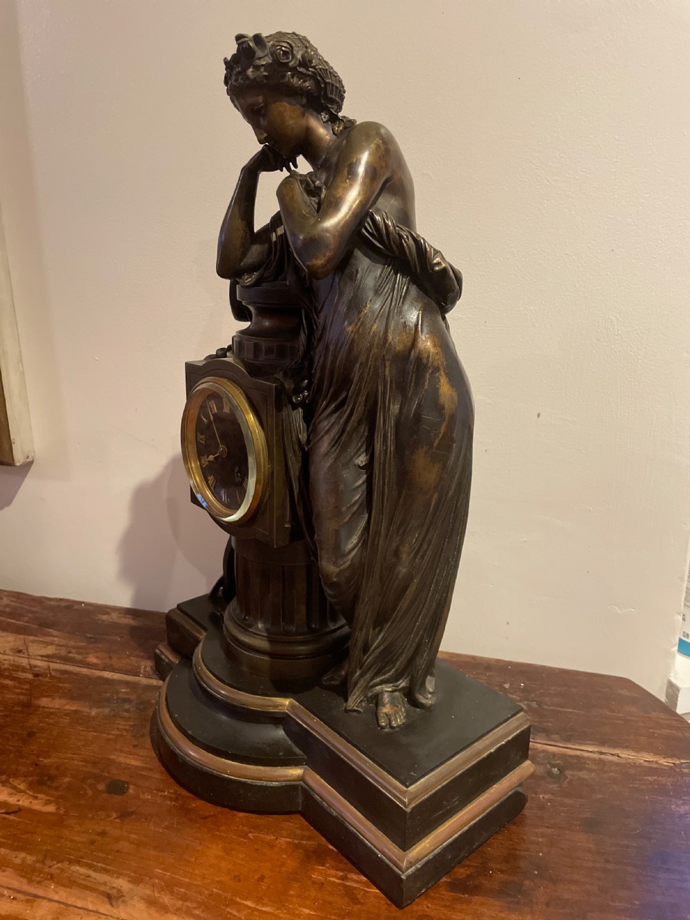 A late 19th-century French dark patinated bronze mantel clock depicting a classical draped female figure leaning upon a column containing a round dial with Roman numerals. View V