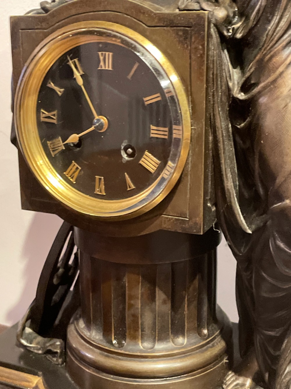 A late 19th-century French dark patinated bronze mantel clock depicting a classical draped female figure leaning upon a column containing a round dial with Roman numerals. View VI