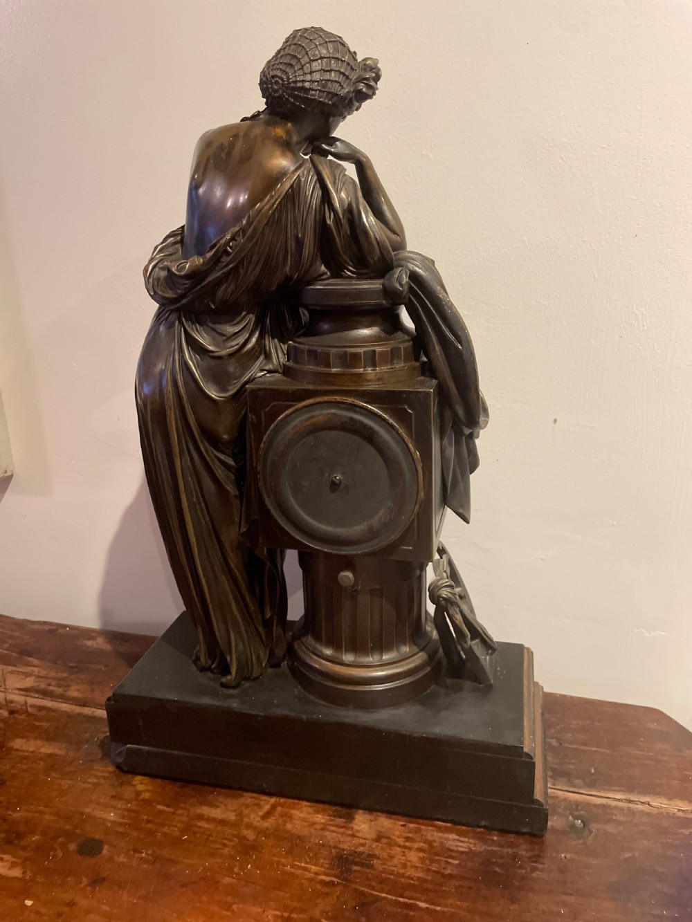 A late 19th-century French dark patinated bronze mantel clock depicting a classical draped female figure leaning upon a column containing a round dial with Roman numerals. View XII