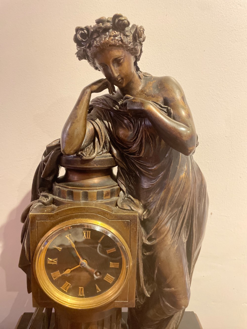 A late 19th-century French dark patinated bronze mantel clock depicting a classical draped female figure leaning upon a column containing a round dial with Roman numerals. View XIV