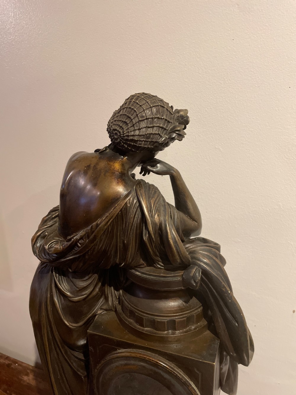 A late 19th-century French dark patinated bronze mantel clock depicting a classical draped female figure leaning upon a column containing a round dial with Roman numerals. View XVIII