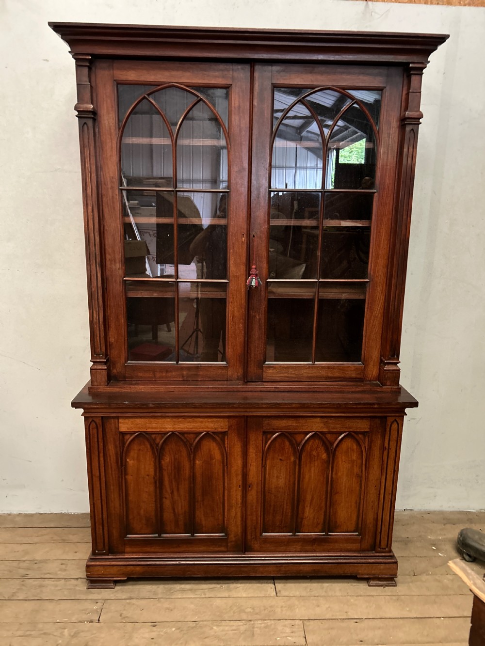 A dark George IV rosewood two-tier bookcase featuring upper glazed doors with Gothic lancet arches and lower panelled doors with tracery.