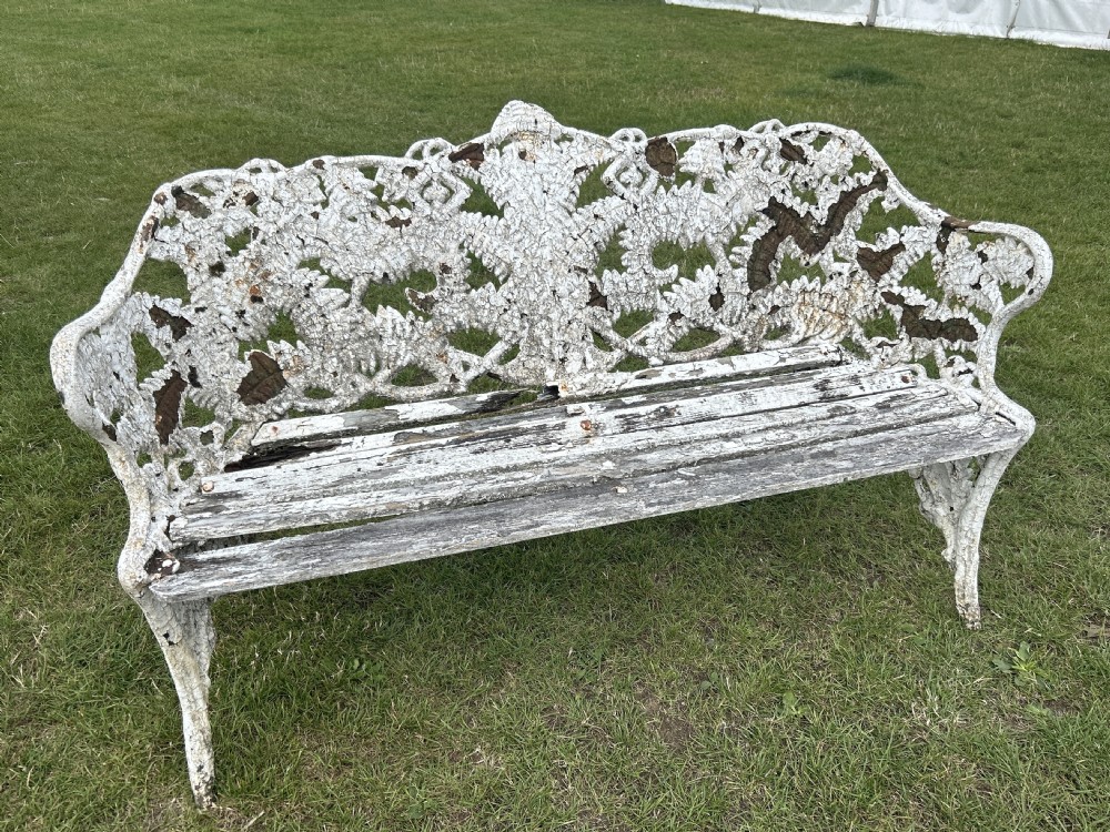 A Victorian white painted cast iron garden bench featuring detailed fern and blackberry motifs on the backrest and a wooden slatted seat.