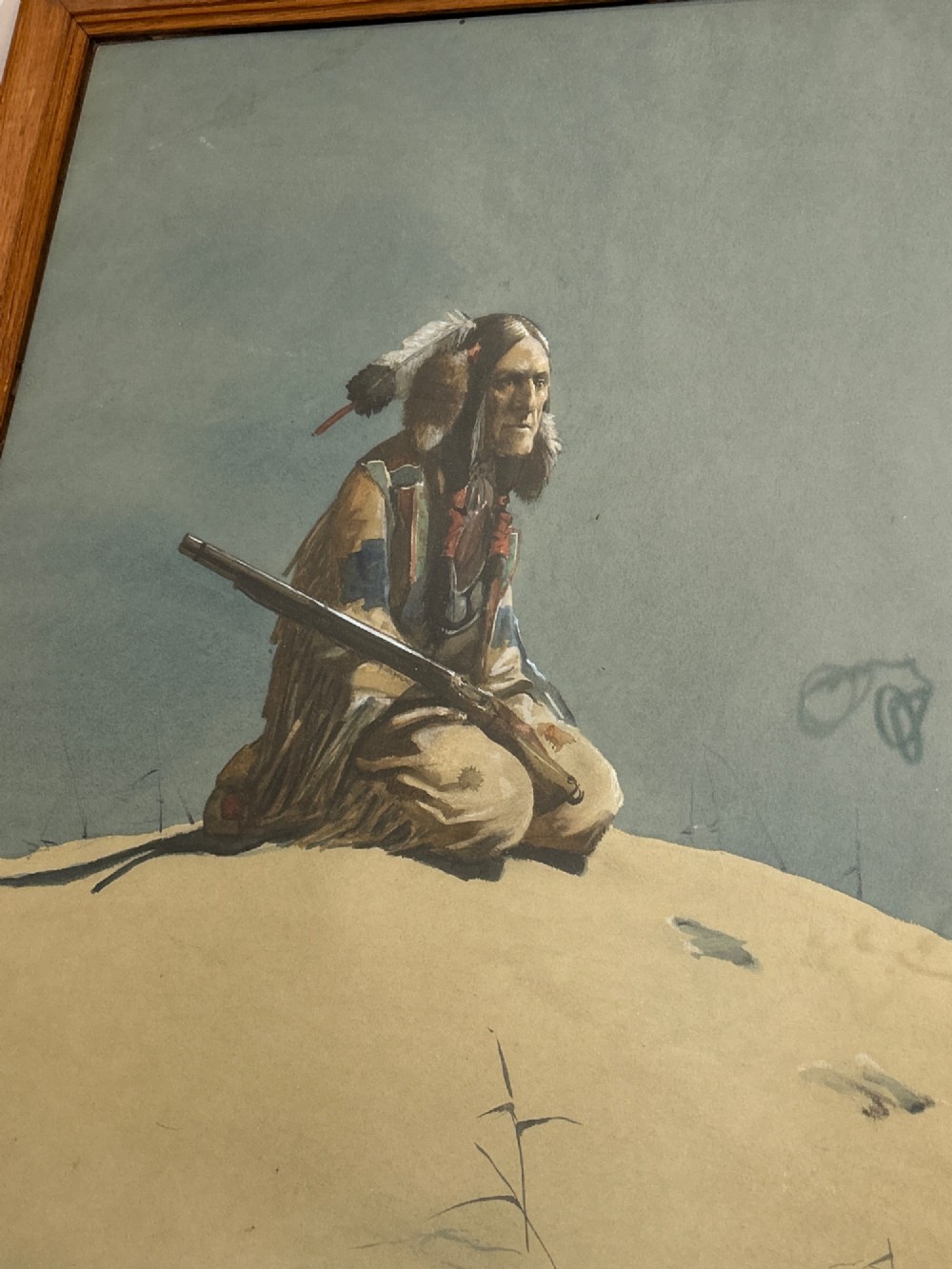 A framed watercolour painting depicting a Native American figure seated on a grassy mound holding a rifle against a muted blue sky. View IX