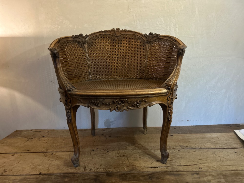 A 19th-century French Louis XV style Corbeille armchair featuring a curved hand-woven cane backrest, carved wooden frame with cabriole legs, and a beige upholstered seat cushion. View III