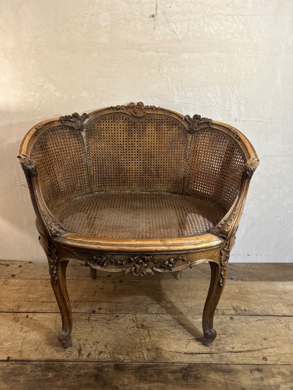 A 19th-century French Louis XV style Corbeille armchair featuring a curved hand-woven cane backrest, carved wooden frame with cabriole legs, and a beige upholstered seat cushion. View IV