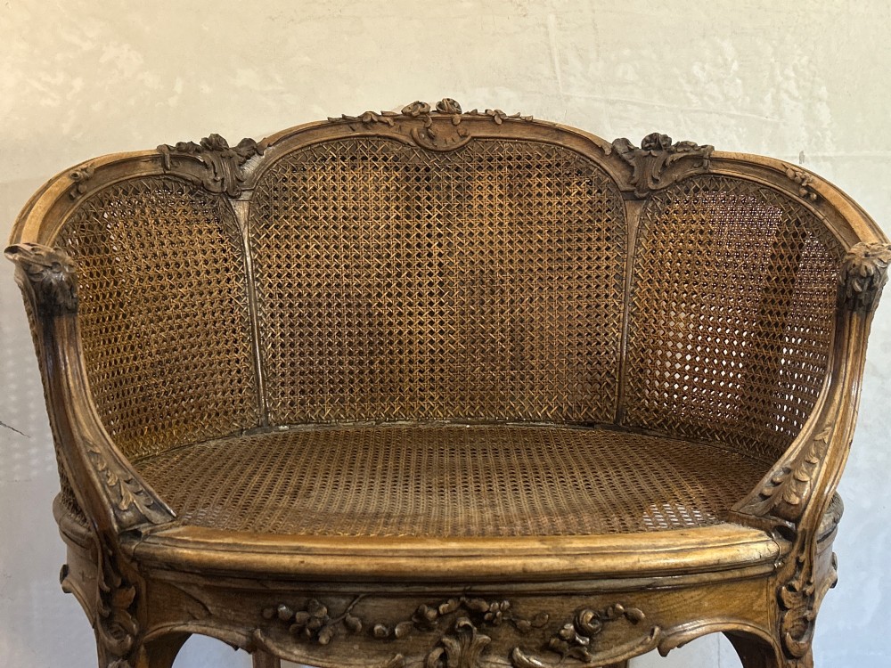 A 19th-century French Louis XV style Corbeille armchair featuring a curved hand-woven cane backrest, carved wooden frame with cabriole legs, and a beige upholstered seat cushion. View V