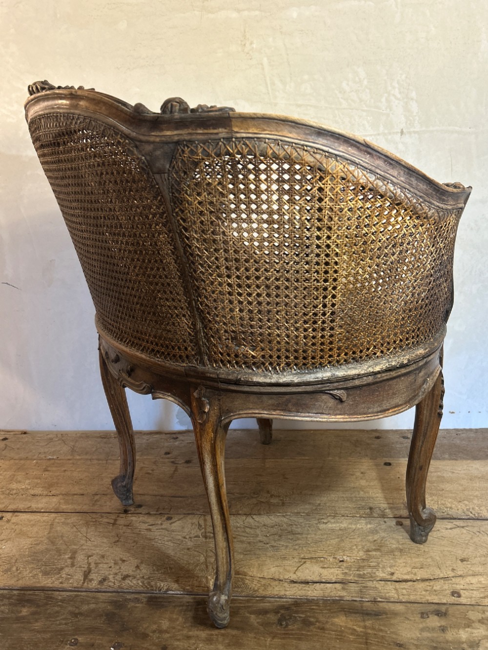 A 19th-century French Louis XV style Corbeille armchair featuring a curved hand-woven cane backrest, carved wooden frame with cabriole legs, and a beige upholstered seat cushion. View IX