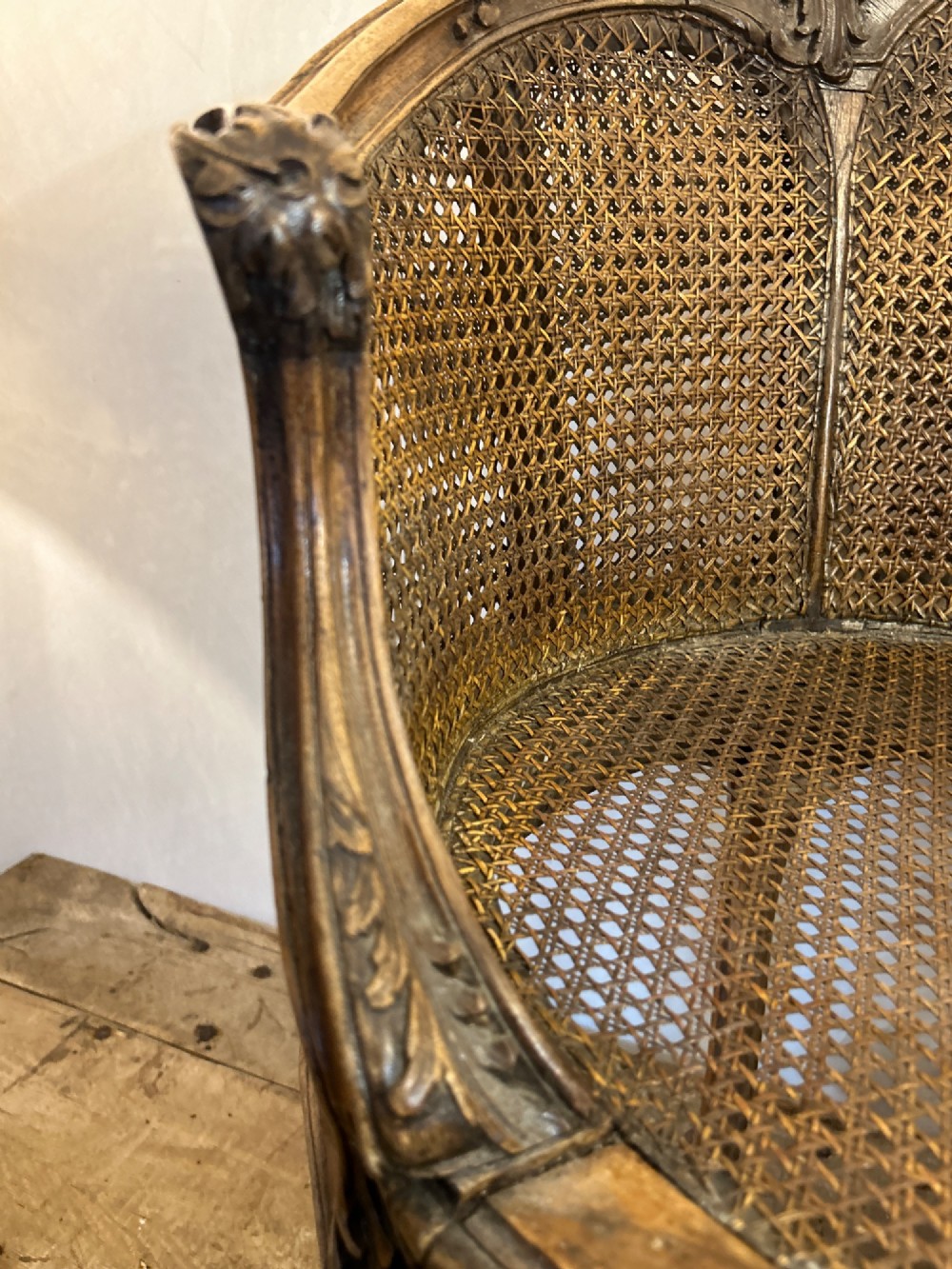A 19th-century French Louis XV style Corbeille armchair featuring a curved hand-woven cane backrest, carved wooden frame with cabriole legs, and a beige upholstered seat cushion. View XIII