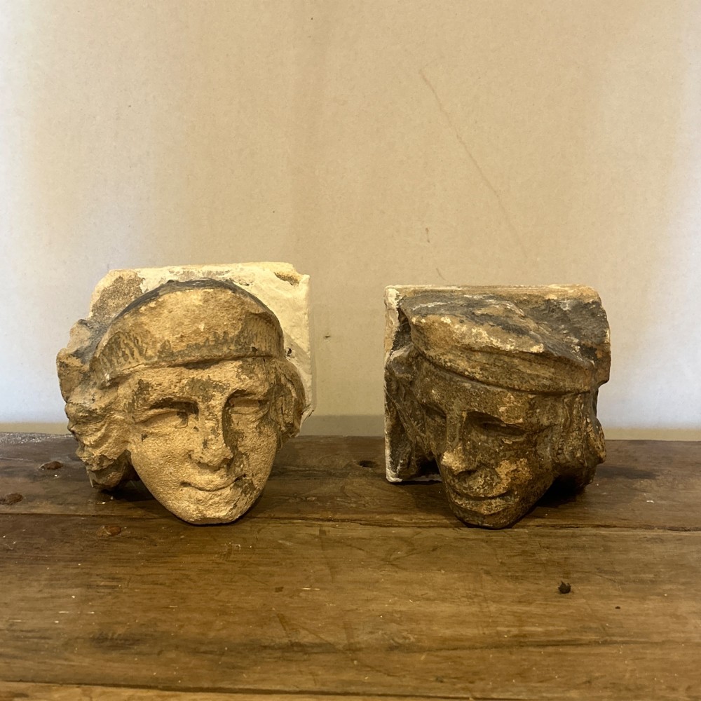 A pair of 15th-century carved limestone corbels depicting human heads with weathered facial features and period headwear.