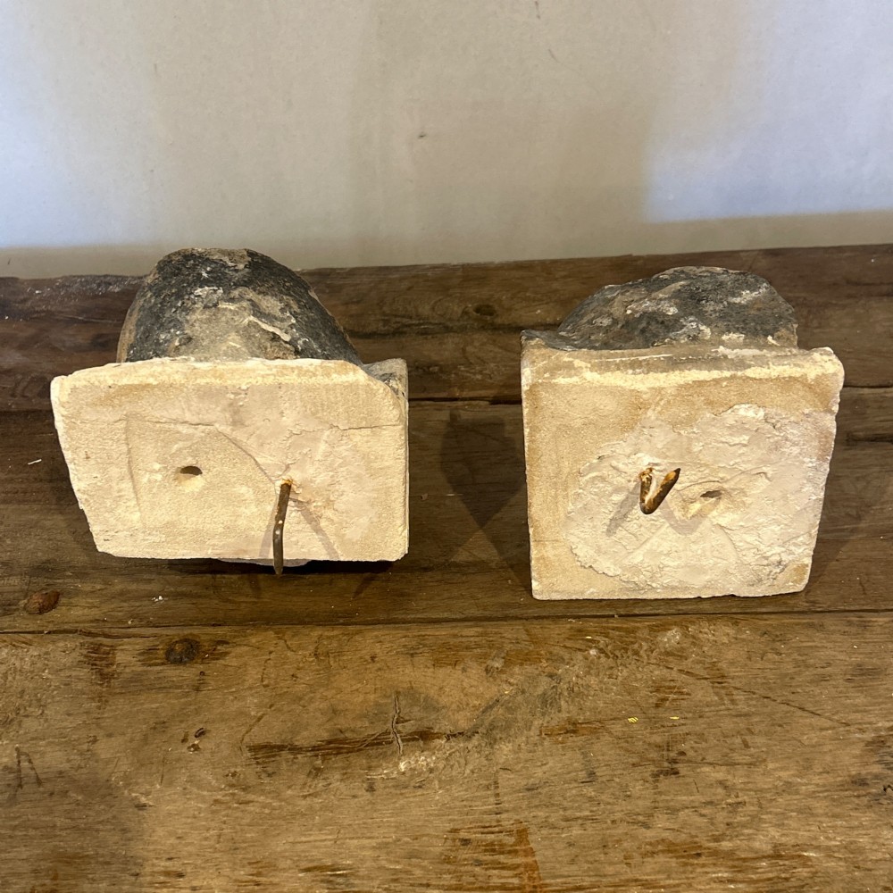 A pair of 15th-century carved limestone corbels depicting human heads with weathered facial features and period headwear. View II